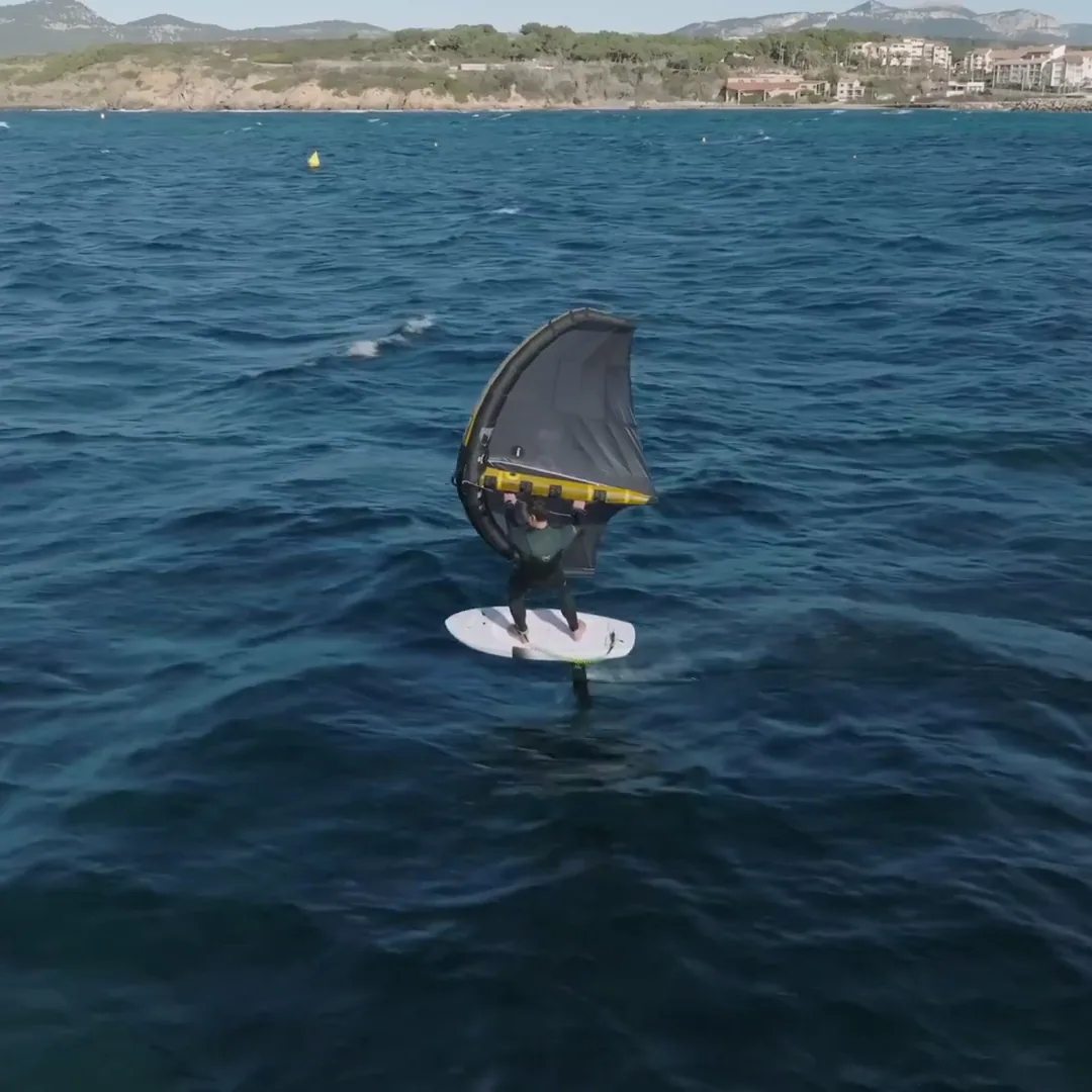 Rider en wingfoil avec aile F-One Strike V5 noire et jaune sur mer agitée