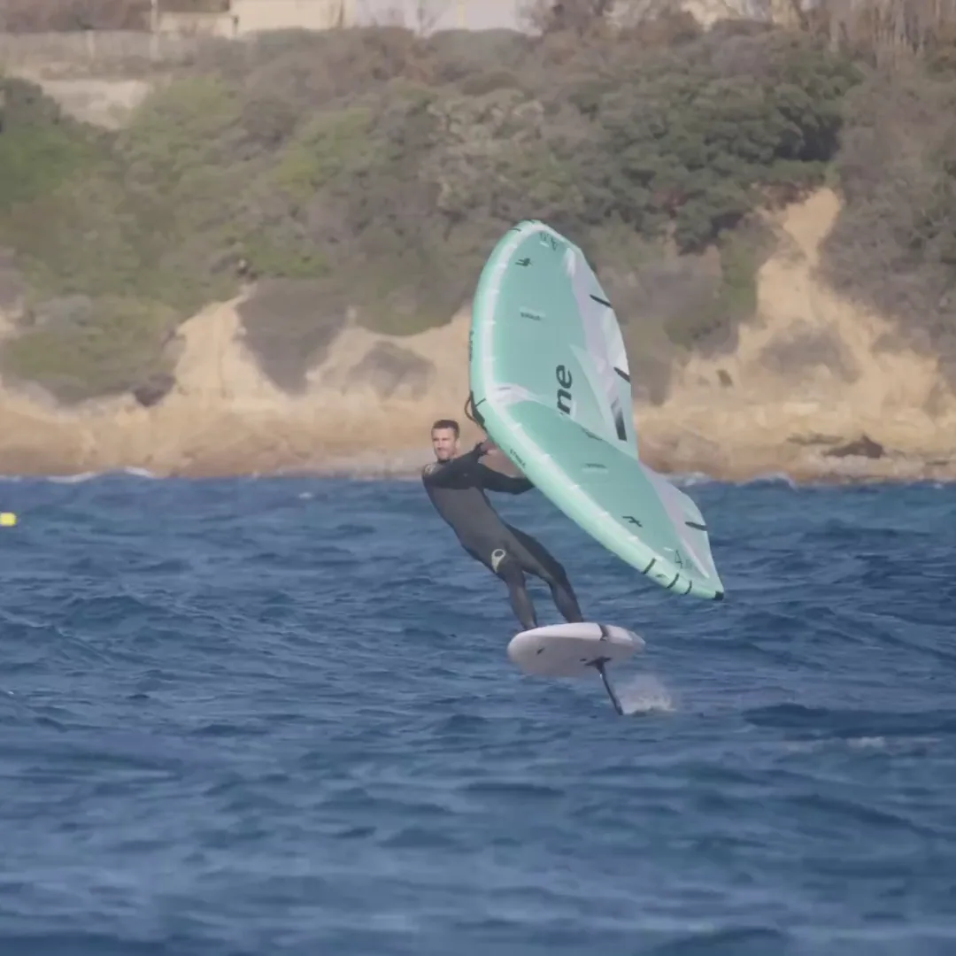 Rider en combinaison noire avec aile Strike V5 turquoise devant côte rocheuse