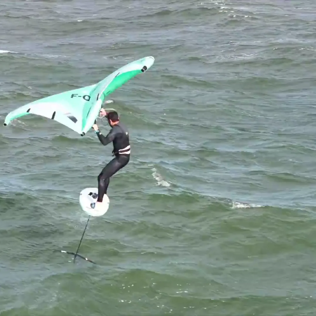 Rider effectuant un saut en wingfoil avec aile F-One Strike V5 verte et blanche