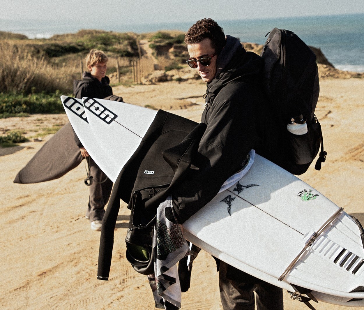 Surfer carrying their ION wetsuit and board on the beach