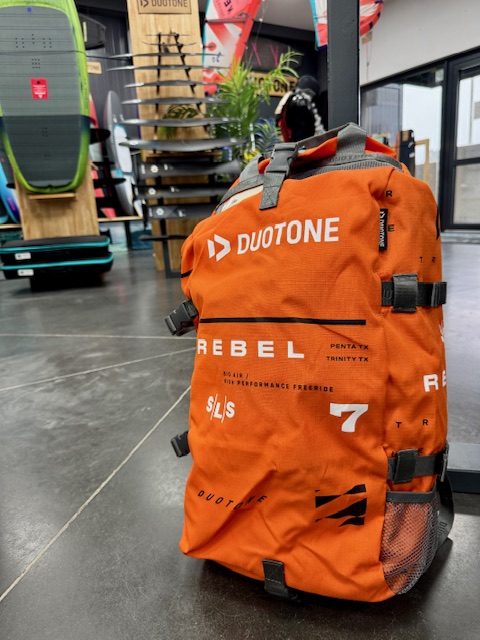 Orange storage bag for the Rebel SLS 2025, with a watersports shop in the background.