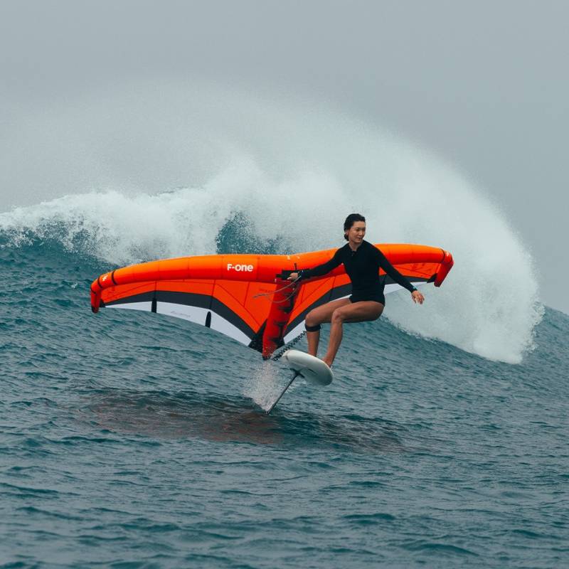 Rider en foil utilisant la F-ONE Strike V5 orange dans les vagues, aile puissante idéale pour surf, vitesse et cap performant