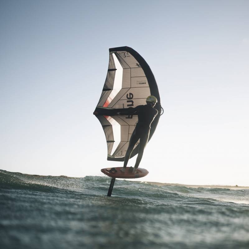Rider en foil avec la F-ONE Swing V5 noire, en navigation fluide sur plan d’eau calme, aile réactive et compacte pour transitions rapides